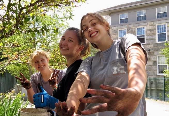 Three young ladies smiling and showing dirty hands at a work project, weeding flower beds