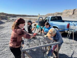 group of team members put gravel through a large screen to sift out the smaller pieces