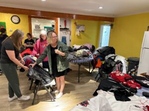 women sort through piles of donated clothing on tables and chairs