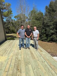 three men standing on a partially finished deck